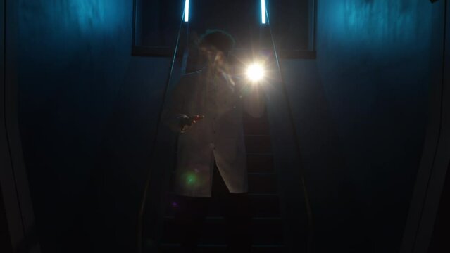 Caucasian man walking downstairs to examine suspicious noise and activity. Young professional in white uniform looking around with a flashlight. High quality 4k footage