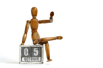 October 05, wooden calendar with mannequin sitting on it on white background. Calendar date.