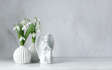 Praying angel figurine and snowdrops flowers on table, abstract light background. symbol of faith in God, christianity. Religious church holiday, Easter, Feast of Annunciation to Blessed Virgin Mary - obrazy, fototapety, plakaty