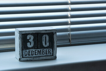 Morning December 30 on wooden calendar standing on window with blinds.