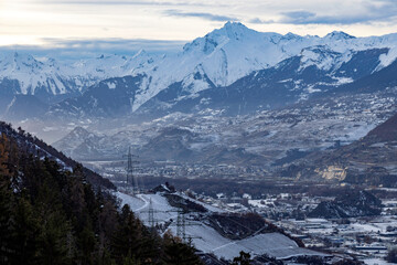 swiss mountains in the winter, the Rhone valley with the city of Sion, some villages, the highway, railway, pylons and a high voltage line - 691174042