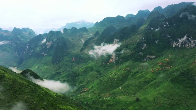 Drone of green mountains, clouds and nature for travel background, tourism location and explore or adventure. Aerial view of landscape, countryside roads and hiking path in Vietnam, Ma Pi Leng Pass