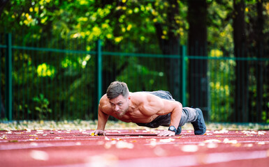 Man Building Strength and Endurance on the Track. A man is doing push ups on a track