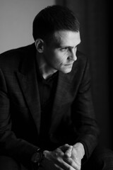 Portrait of a young man in a plaid suit on a chair. Business portrait. 