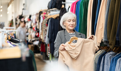 Elderly woman buyer chooses sweatshirt in clothing store..