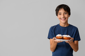 Little boy in kipa holding plate with tasty donuts on grey background. Hanukkah celebration
