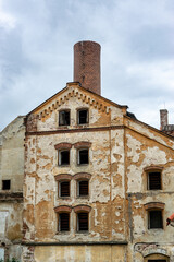An old ruined factory with a chipped facade and broken windows. A large brick chimney on the roof.