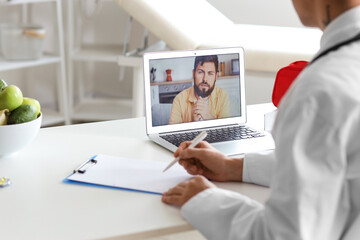 Young doctor video chatting with patient on laptop in office, closeup