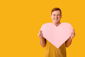 Happy young man with pink paper heart on yellow background