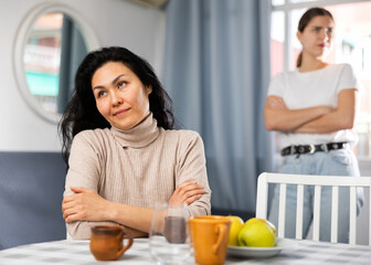 Upset disappointed woman sitting at home while girl calming her, asking to forgive after argument