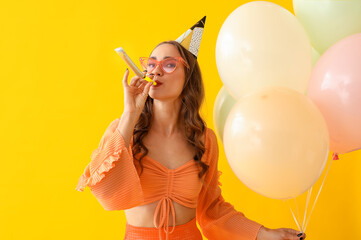 Beautiful young woman with party whistle and air balloons celebrating Birthday on yellow background