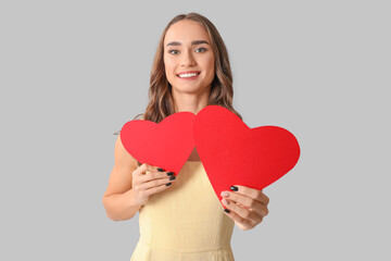 Beautiful young woman with red paper hearts on grey background