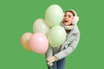 Fototapeta na wymiar Beautiful young woman in warm winter clothes with balloons on green background