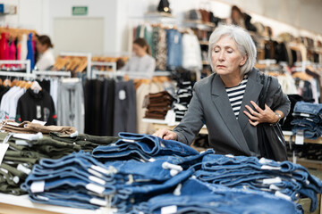 Elderly woman carefully chooses jeans in a clothing boutique