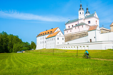 Cyclist riding bike along church in Camaldolese monastery complex on the Wigry lake peninsula,...