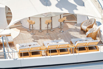 Close up footage of a relaxation area on the open teak deck of an expensive megayacht at sunny day, with awnings stretched over the deck to protect from the sun, wealth life, table and chairs