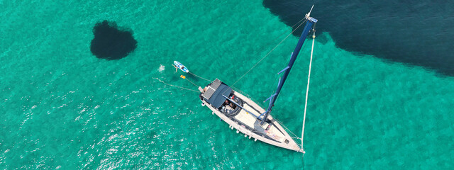 Aerial drone ultra wide panoramic photo of beautiful sail boat with white sails anchored in tropical exotic bay with emerald clear sea