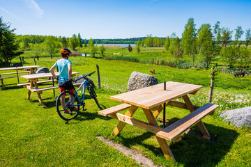 Woman cyclist standing between tables of a bar near lake shore during spring in Wigry National Park, Podlasie, Poland