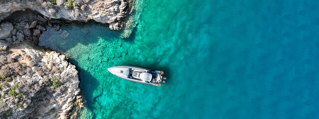Aerial drone top down ultra wide photo with copy space of inflatable speed boat anchored in tropical exotic rocky island with emerald crystal clear sea
