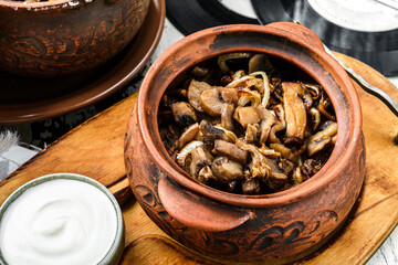 Baked mushrooms with onions in clay pot with sour cream on wooden board. Homemade food, close up