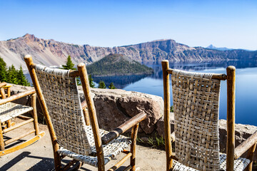 Rocking chairs overlooking the rim of the caldera with Wizard Island in the background in Crater Lake National Park, Oregon United States on a clear summer day. - obrazy, fototapety, plakaty