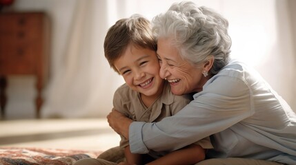 A joyful boy sits on the floor, embracing his grandmother in a heartwarming hug. Their beaming smiles capture the pure and unconditional love.