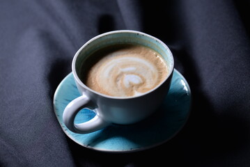 Cup of coffee on a black background, top view. White cup on textile fabric 