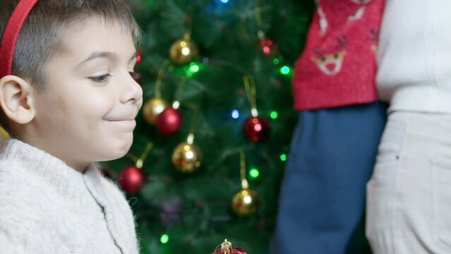 Christmas tree decoration. Happy boy smiling while his dad and brother are putting christmas ornamets on the tree. High quality 4k footage