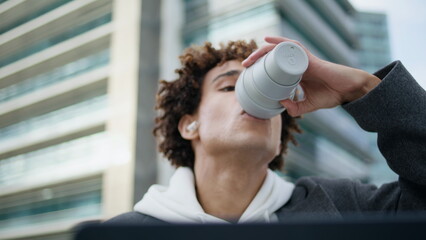 Earbuds hipster sipping coffee at urban place closeup. Student learning laptop