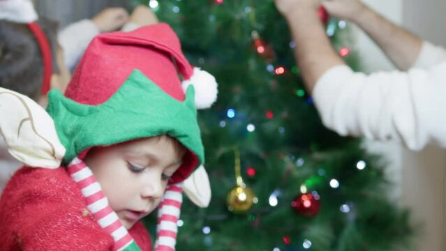 Close up on preschool boy with elf hat. Father and sons decorating christmas tree. Merry christmas. High quality 4k footage