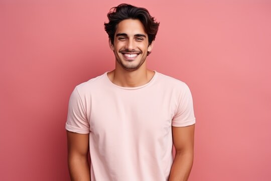 Portrait of a handsome young man smiling at camera while standing against pink background