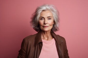 Portrait of beautiful senior woman looking at camera and smiling while standing against pink background