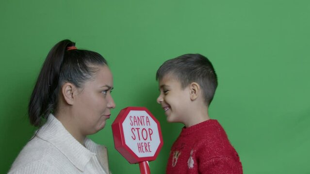 Close up mom and son gets into the funny argument than hug and kiss. Santa stop here sign. Christmas holiday. Isolated on green. High quality 4k footage