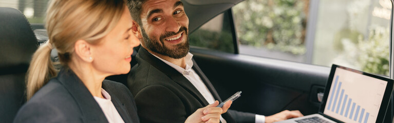 Business colleagues working on laptop while sitting in car backseats. High quality photo