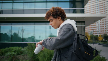 Busy guy checking time at street closeup. Curly student hurry to college outdoor