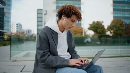 Young freelancer working computer at street closeup. Curly guy chatting laptop