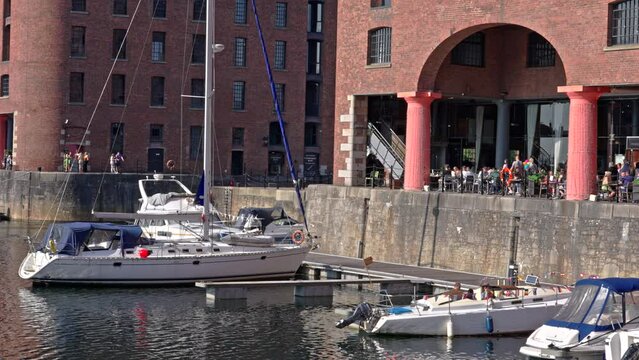 Liverpool, UK - May 20 2023: Boats, yachts docked at Albert Dock next to a covered balcony restaurant full of diners