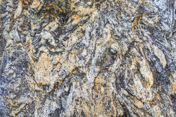 Closeup detail of texture and swirling patterns in a gray, white, and orange rock, as a nature background
