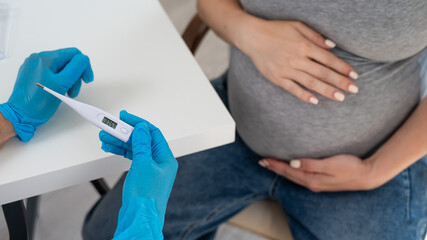 Pregnant woman with fever at doctor's appointment. Therapist holds an electronic thermometer with a temperature of 37.5. 