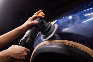 Car detailing - Man with orbital polisher in repair shop polishing car. Selective focus