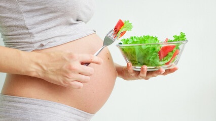 View a pregnant womanholding a bowl with fresh salad, enjoyinghealthy lifestyle during her pregnancy