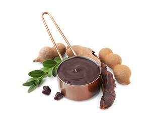 Measuring cup with tasty tamarind sauce, leaves and fresh pods isolated on white