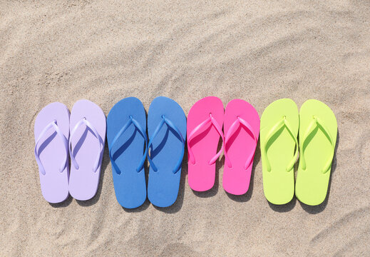 Many stylish colorful flip flops on sand outdoors, flat lay