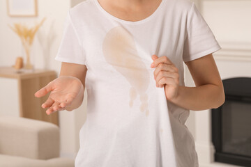 Woman showing stain from coffee on her shirt indoors, closeup