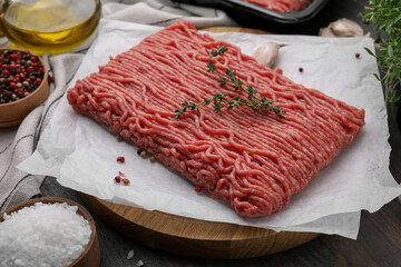 Fresh raw ground meat, thyme and peppercorns on wooden table, closeup