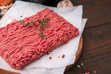 Fresh raw ground meat, thyme and peppercorns on wooden table, closeup