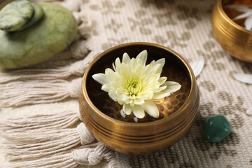 Tibetan singing bowl with water, beautiful chrysanthemum flower and stones on table, closeup