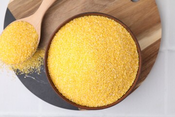 Raw cornmeal in bowl and spoon on white table, top view