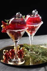 Creative presentation of Christmas Sangria cocktail in baubles and glasses on grey table against black background, closeup
