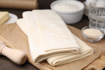 Raw puff pastry dough on wooden table, closeup